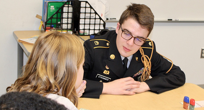 Cadet Strommen discusses a Junior Achievement assignment with a Highland Park Elementary student.