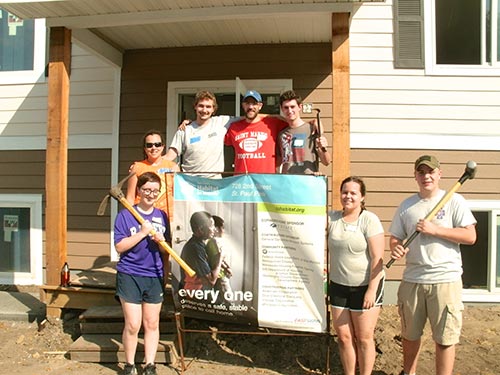 CDH students, faculty, and staff take a break for a group picture outside the home they helped build.