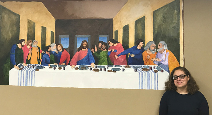 Jessica Lutmer '21 and her painting in the St. Peter Catholic School cafetera.